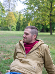 Photo of a young and attractive man sitting on the park smiling and enjoying a sunny day