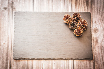 Pine cones on a slate resting on a wooden background with copy space, an autumn background