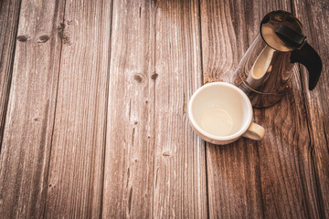 A silver coffee pot and white coffee cup on a rustic wooden background with copy space