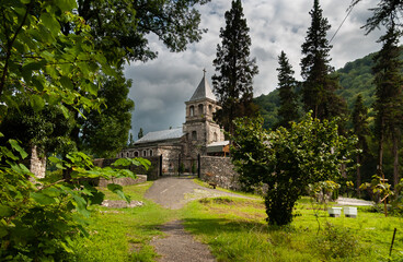Fototapeta na wymiar The temple on the hill, built of brown stone surrounded by forest and green wooded mountains. Abkhazia, the village of Kamany, The burial place of St. John Chrysostom in 407
