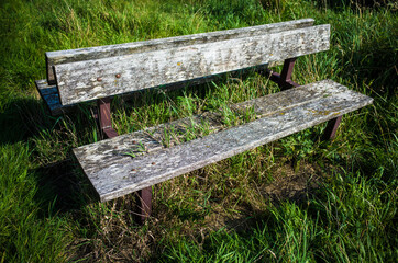 An old, wooden abandoned bench overgrown with weeds.