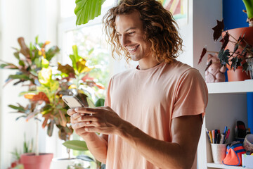 Happy smiling curly man indoors using mobile phone