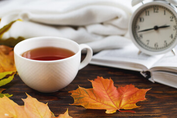 cup of coffee or tea with golden autumn leaves, plaid, alarm clock and book on a wooden background .Fall concept.