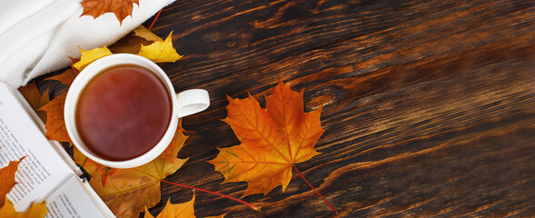cup of coffee or tea with golden autumn leaves, plaid and book on a wooden background .top view....