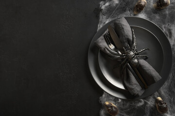 Halloween table setting with skulls , web and spider on black dark table. View from above. Space...