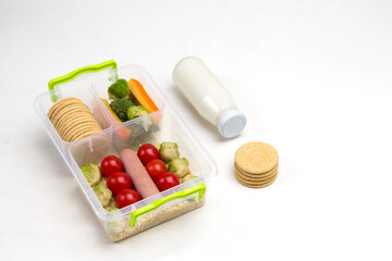 Nutritious lunch box with vegetables and sausage. Bottle of yogurt and cookies