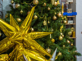 Christmas toy golden star hanging on green branches. close up. yellow balls on the background
