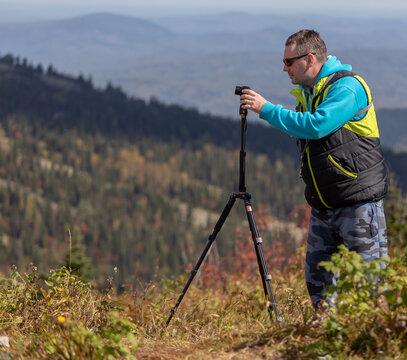 a photographer shoots an autumn landscape with a small camera on a tripod. side view of the process of taking photos from a tripod with a man in the frame
