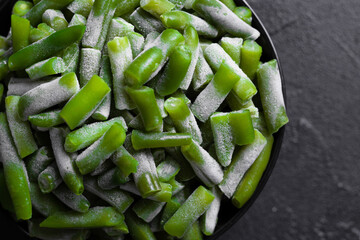 Green beans cut in pieces and frozen in the black bowl on the black marble table. Overhead shot of sprout.