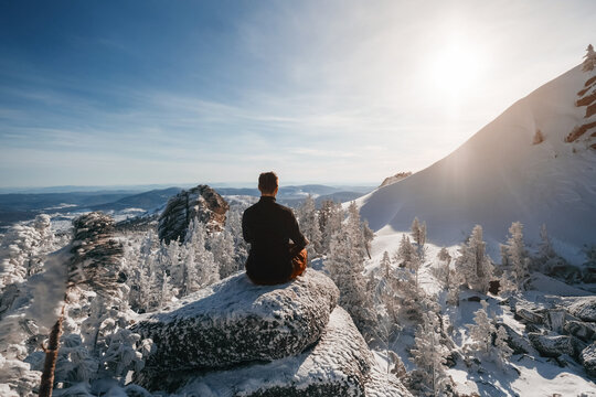 Hiker seating on top of mountain cliff and enjoying the view of valley and winter mountain landscape