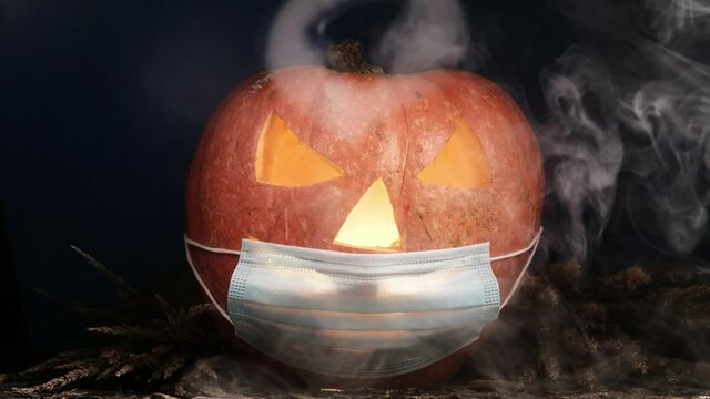 Halloween carved pumpkin glowing with protective medical face mask, coronavirus and quarantine concept, covid-19 halloween costume. eyes change brightness. White smoke.