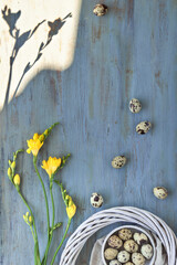 Easter flat lay with quail eggs, heart shape with text Easter. Yellow freesia flowers and rattan wreath.