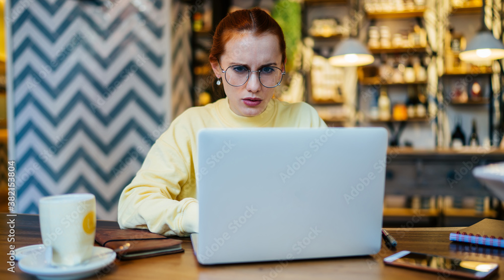 Poster serious woman in glasses solving online problems with system updation on laptop computer during remo