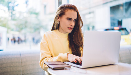 Puzzled female freelancer working remotely with online startup project solving problem with mistakes via laptop application, Caucasian red hair woman searching website for download media file