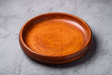 Empty round handcrafted brown wooden plate on stone concrete background, angle view