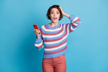 Photo of lovely lady hold telephone open mouth arm head wear striped pullover red trousers isolated blue color background