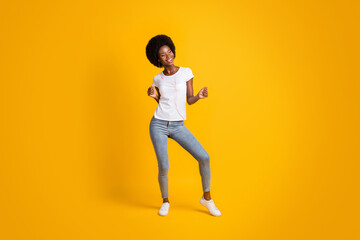 Fototapeta na wymiar Full length body size photo of smiling girl with black skin listening music dancing keeping hands up isolated on bright yellow color background