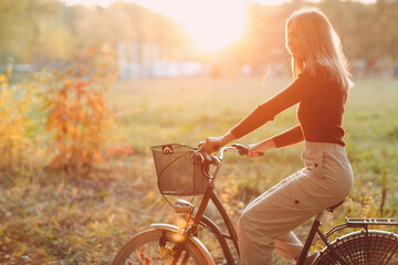 Happy active young woman riding vintage bicycle with basket in autumn park at sunset