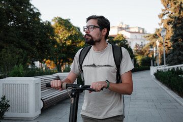 Attractive man riding a kick scooter at cityscape background.