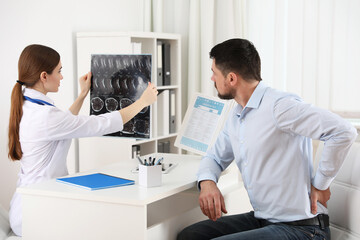 Orthopedist showing X-ray picture to patient at table in clinic