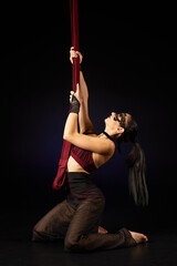 Brunette beautiful caucasian woman in Lace mask doing circus tricks on red silks isolated on black background.