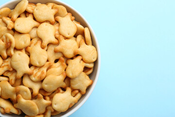 Delicious goldfish crackers in bowl on light blue background, top view. Space for text