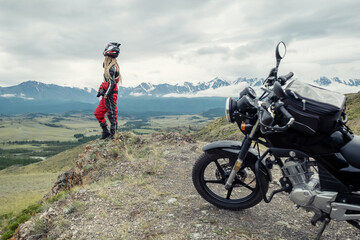 Female rider standing near her motorcycle  in mountains landscape. Long travel in Altai mountain in Russia