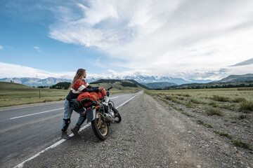 Female rider standing near her motorcycle  in mountains landscape. Long travel in Altai mountain in...