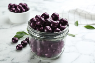 Fresh acai berries in glass jar on white marble table, closeup