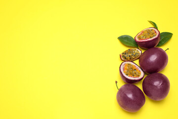 Fresh ripe passion fruits (maracuyas) with green leaves on yellow background, flat lay. Space for text