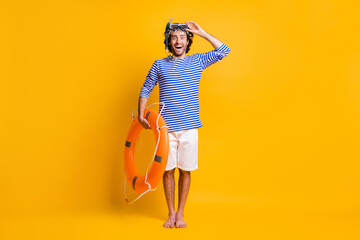Fototapeta na wymiar Ful size photo of excited guy hold life buoy touch scuba goggles wear blue striped shirt shorts isolated on yellow color background