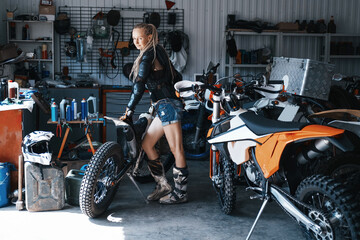 Female wearing shorts, moto boots and motorcycle .armor resting in garage with enduro motorcycles