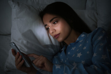 Young woman using mobile phone in dark bedroom