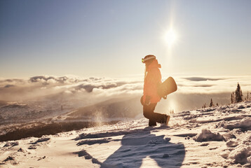 Female snowboarder holding snowboard standing on mountain slop, preparing to snowboarding. Sunny...