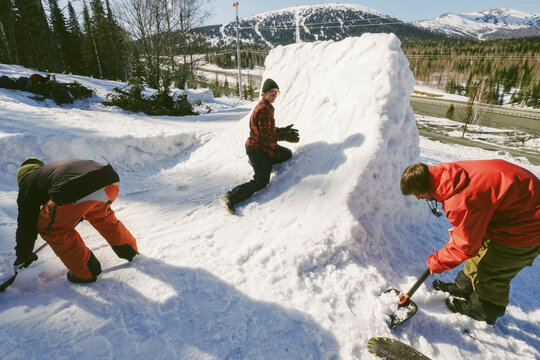 Friends snowboarders build quarter pipe snowboard outdoor near ski resort in mountains. Sunny winter day