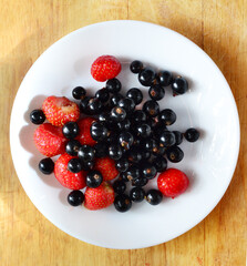 strawberries and black currants on a white plate and wooden table, harvesting, fresh and healthy vitamin-rich food