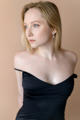 Fototapeta premium Graceful young woman in a black top posing against beige wall.