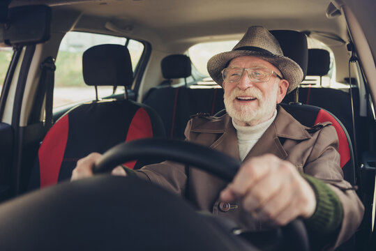 Close-up portrait of his he nice experienced cheerful cheery glad grey-haired man driving car in traffic jam holding steering wheel enjoying far way road