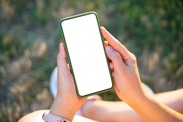 Trendy smartphone device mock up. Hipster girl holding mobile phone with blank screen with copy space for design or logo outdoors, sunny weather
