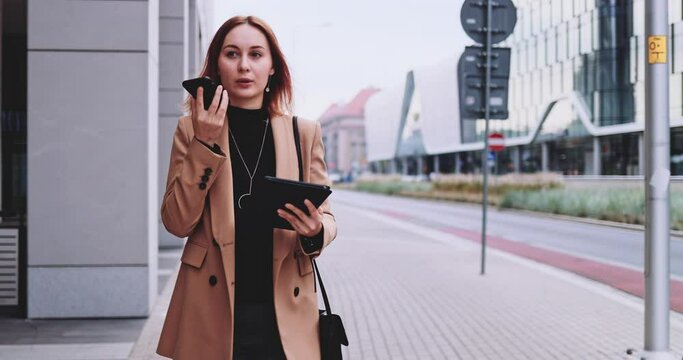 Business Woman With Tablet Talking On Smartphone Walking In The City. SLOW MOTION Gimbal Stabilized. Young Professional Female rushing to the office in the morning. Female entreprneur networking