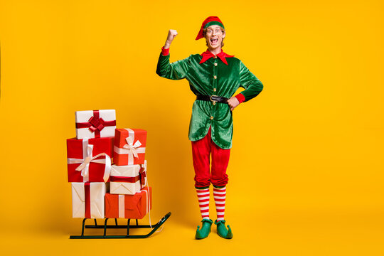 Full length body size view of his he nice attractive cheerful cheery funny guy elf carrying gifts on sledge having fun christmastime isolated over bright vivid shine vibrant yellow color background