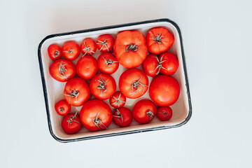 Fresh red tomatoesof different sizes in an enamel bowl on the table, top view