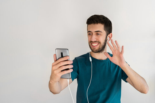 Young man with a big smile on his face, doing a video call and waving his hand to the camera.