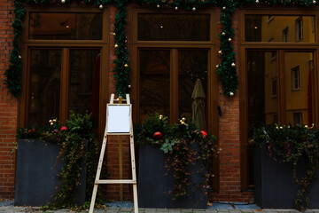 Fototapeta na wymiar Traditional Christmas decorations outside the cafe. Christmas wreaths on the windows and decorated lamppost with garlands near the building.
