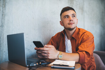 Dreamy guy with smartphone sitting at table