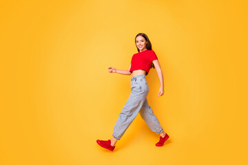 Fototapeta na wymiar Full length photo of lady making step walking down street wear red crop top jeans shoes isolated yellow color background