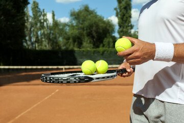 Sportsman with racket and tennis balls at court, closeup