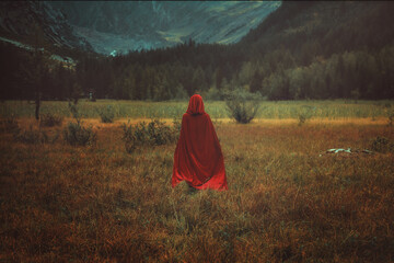 Woman with red cloak in a mountain valley