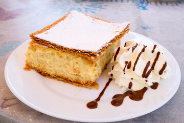 Traditional Balkan and Hungarian sweet dessert - homemade freshly baked krempita cream pie with milky filling, crispy corn with sugar powder and whipped cream