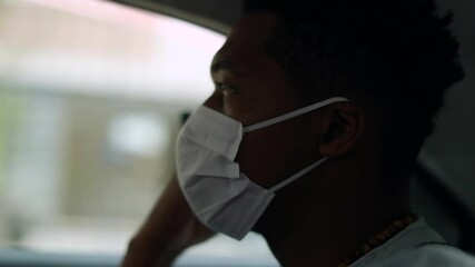 Black man in backseat car looking at cellphone screen wearing face mask prevention against pandemic
